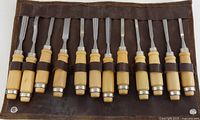 12 chisels with wood handles secured in leather roll, blades visible