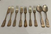 Flatware laid out showing eight forks and two spoons with Fiddle pattern handles