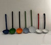 Seven ladles standing upright showing bowl shape, colour and handles