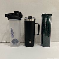 Three portable beverage containers lined up: Rangers protein shaker, TAL travel mug, Starbucks tumbler