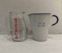 Front view of glass Evenflo measuring cup and white enamel measuring pitcher