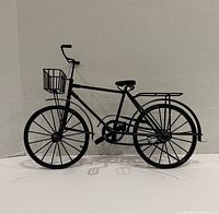 Full view of black metal bicycle model showing basket, frame, wheels and racks