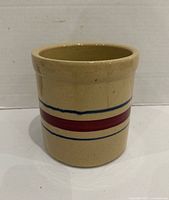 Front view of cylindrical tan crock with red and blue stripes