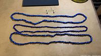 Three blue bead necklaces and pair of blue bead stud earrings laid out on table