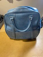 Front view of light blue vinyl travel bag showing handles and exterior pocket