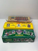 Three boxed baseball card sets stacked: tan Fleer, yellow Score 1990, green Upper Deck 1990