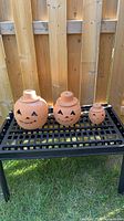 Front view of three terra cotta jack-o-lantern pumpkins on metal bench