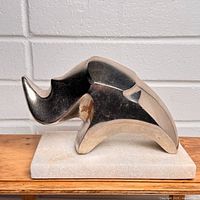 Front-side view of polished metal rhino on marble base