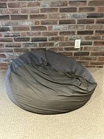 Front view of grey bean bag chair against brick wall
