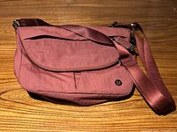 Front view of purple nylon Lululemon crossbody purse on wooden surface