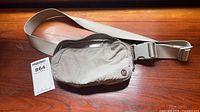 Front view of pale grey Lululemon crossbody bag with strap and logo badge visible