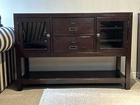 Front view of dark wood console cabinet showing glass doors, drawers, and bottom shelf
