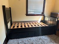 Full view of black wooden trundle bed frame showing slat base, headboard, side panel, drawers