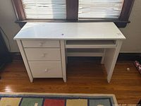 Front view showing entire white desk, three drawers left, keyboard tray right.