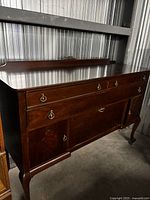 Front view of hardwood sideboard showing drawers, cabinets, brass pulls, cabriole legs