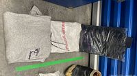 All three folded garments: grey sweatshirt, white T-shirt, black sweatshirt in plastic