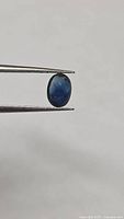 Oval blue sapphire held in tweezers, front view
