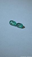 Pair of loose cushion cut emeralds side by side on neutral background
