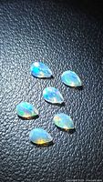Six pear-cut opals on black textured background showing play of color