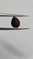 Pear cut orange tourmaline held by tweezers side profile