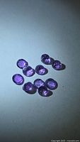 Group of ten round faceted purple amethyst gemstones on white background