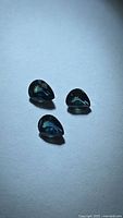 Three pear-cut teal blue-green sapphires on neutral background