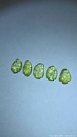 Five carved leaf-cut lemon-lime tourmaline gemstones on neutral background