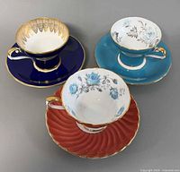 Three teacup and saucer sets showing colors and gilt trim
