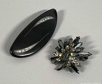 Front view of both brooches: black oval with MOP inlay and Sherman rhinestone floral