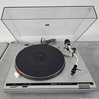 Turntable without dust cover showing platter, tonearm, controls and power cord