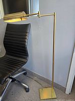 Full view of brass floor lamp beside chair showing base, stem, arm, shade