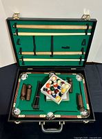 Open briefcase showing pool table, cue sticks in lid, balls and legs