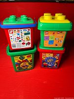 Four Lego/Duplo storage bins stacked, showing colors and printed set numbers