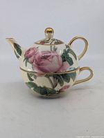 Teapot stacked on teacup showing full set, rose design and gold accents