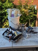 Overall lot on table showing bucket, roller covers, brushes, roller frames, caulk gun