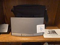 Front view of Bose SoundDock Portable speaker dock with carrying bag behind and manual in foreground