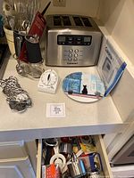 Countertop view showing toaster, utensil holder, timer, plate, owl trivet, grinder and open drawer of utensils