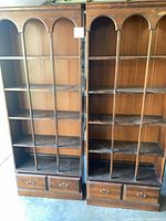 Front view of both matching tall walnut-finish bookcases showing shelves and lower drawers