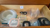 Drawer view showing nested plastic bowls with teal lids, glass containers with coral/yellow/black lids, plastic containers and lids