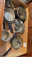 Drawer view of cookware set showing pots, pans, lids with purple handles