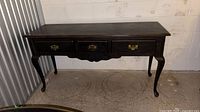 Front full view of dark wood console table with three drawers and cabriole legs