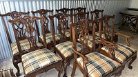 Front view of all ten carved dining chairs showing plaid seats and carved backs
