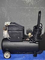 Overall view of portable air compressor showing tank, motor housing, wheels, handle and coiled hose