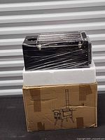 Stove in plastic wrap on foam block atop original box showing line art of assembled stove