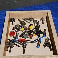 Top view of wooden tray containing assorted 1/4" shank router bits with various profiles and colored sleeves