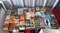 First tabletop shot showing approximately 30 thriller paperbacks by top-selling authors