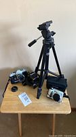All items on table: Canon film camera with lens, Olympus digital camera, tripod, cases, caps, strap