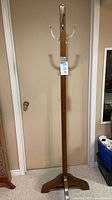 Full view of coat rack showing height, tripod base, wood finish