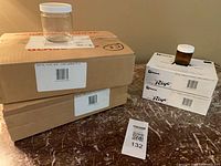 Sealed cartons of 250 mL flint jars, cartons of 50 mL amber jars, sample jars displayed