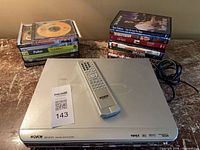 DVD player with remote, power cord and stacked DVDs visible